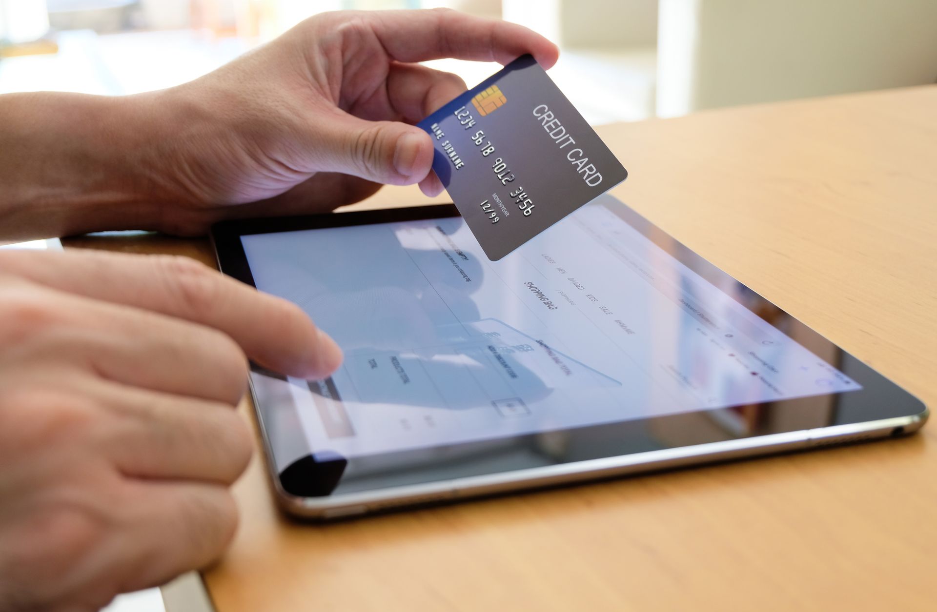 Person holding credit card over tablet, completing online purchase.