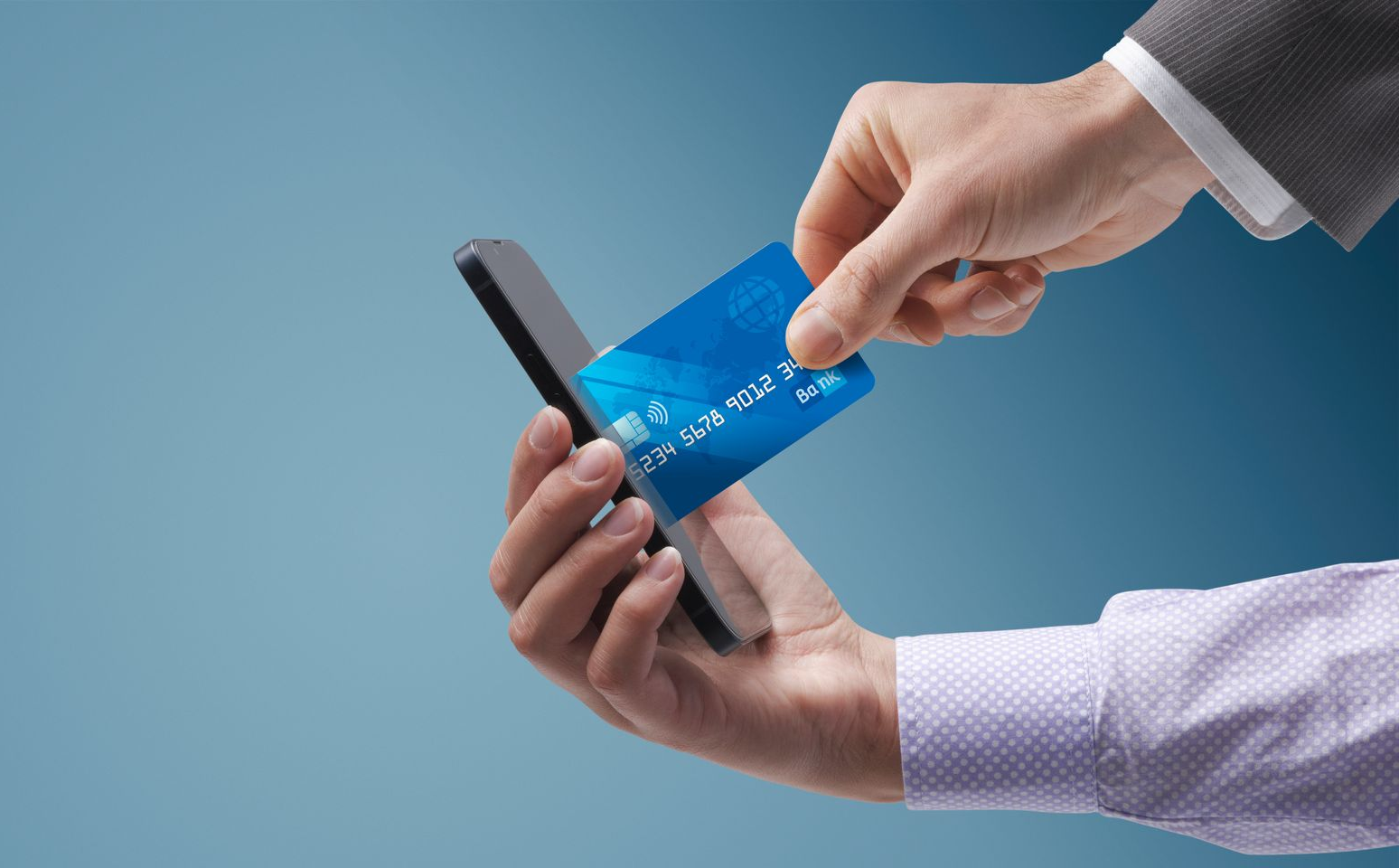 Hand holding a blue credit card near a smartphone, possibly for payment.