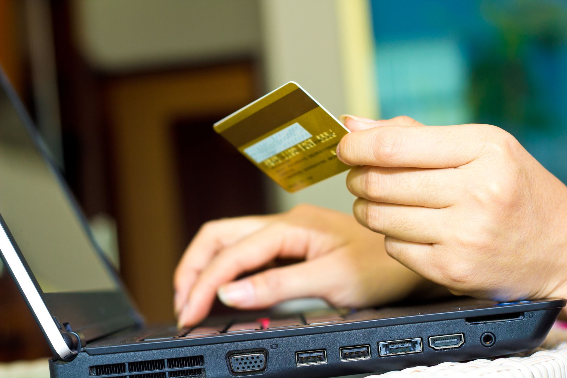Person using a laptop with one hand holding a gold credit card while typing.
