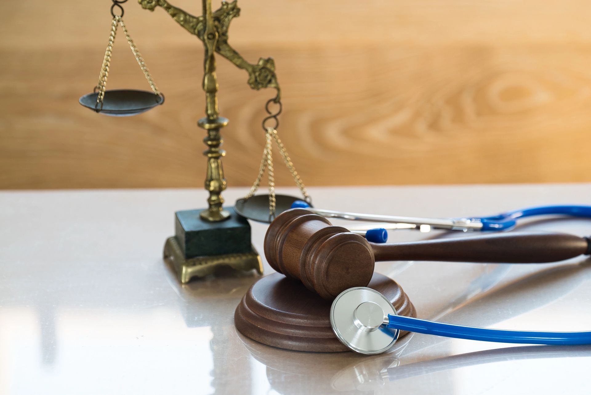 Un martelletto da giudice in legno, uno stetoscopio con tubo blu e una bilancia di ottone su una superficie chiara.
