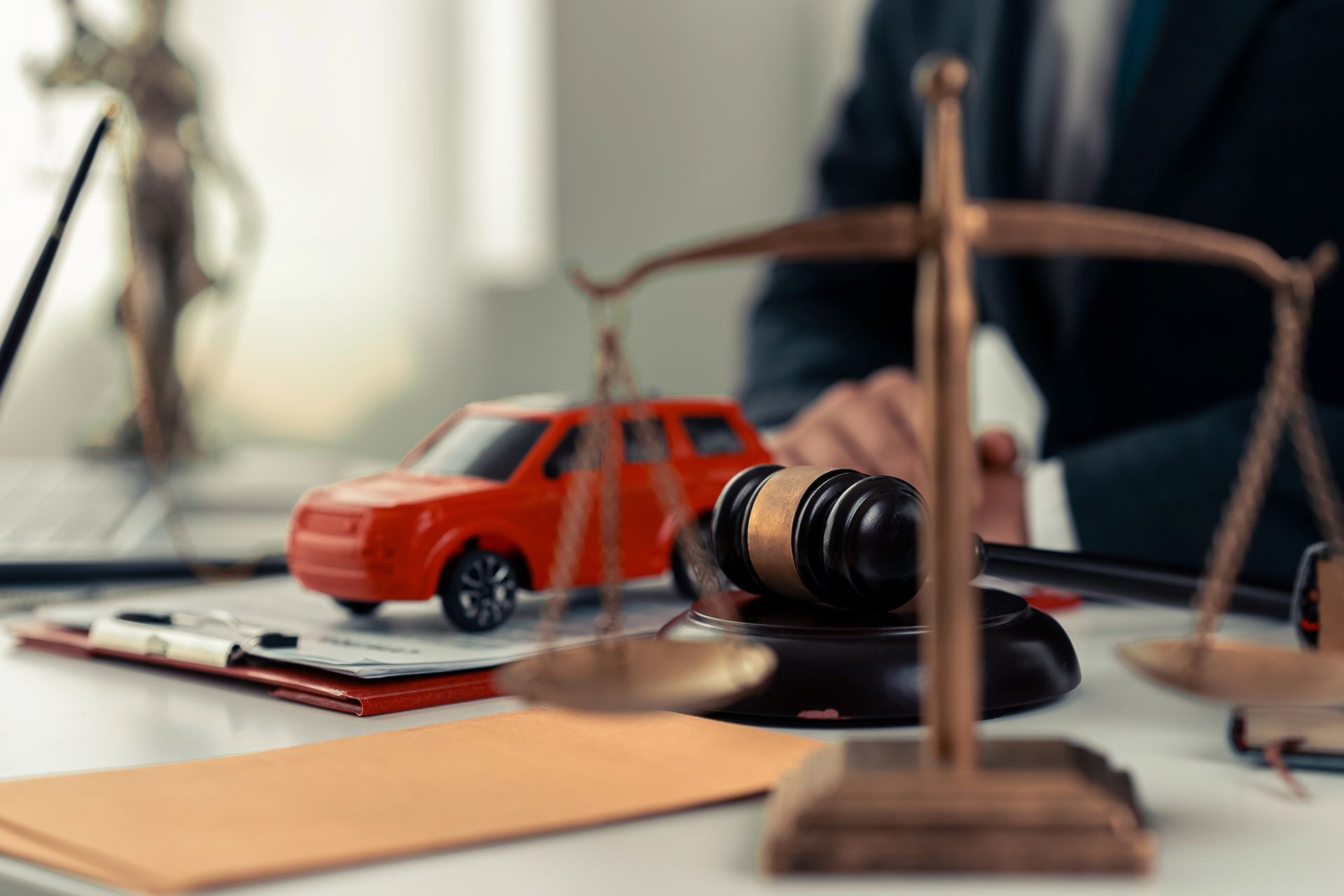 Un'ambientazione legale con un'automobilina giocattolo rossa, un martelletto e una bilancia di ottone su una scrivania di fronte a un avvocato.