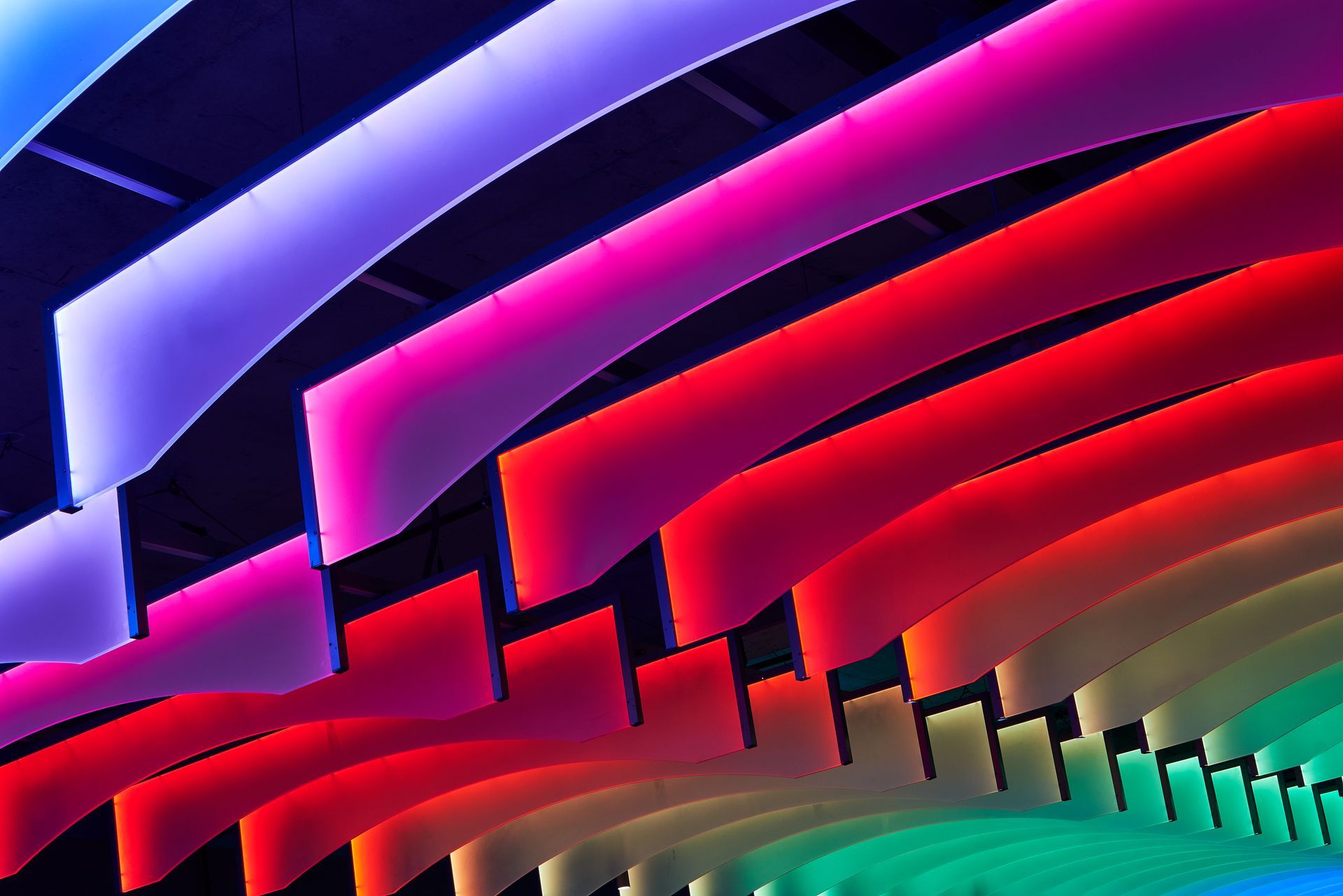 Colorful, illuminated ribbons in shades of purple, pink, red, and green, curving across a dark ceiling.