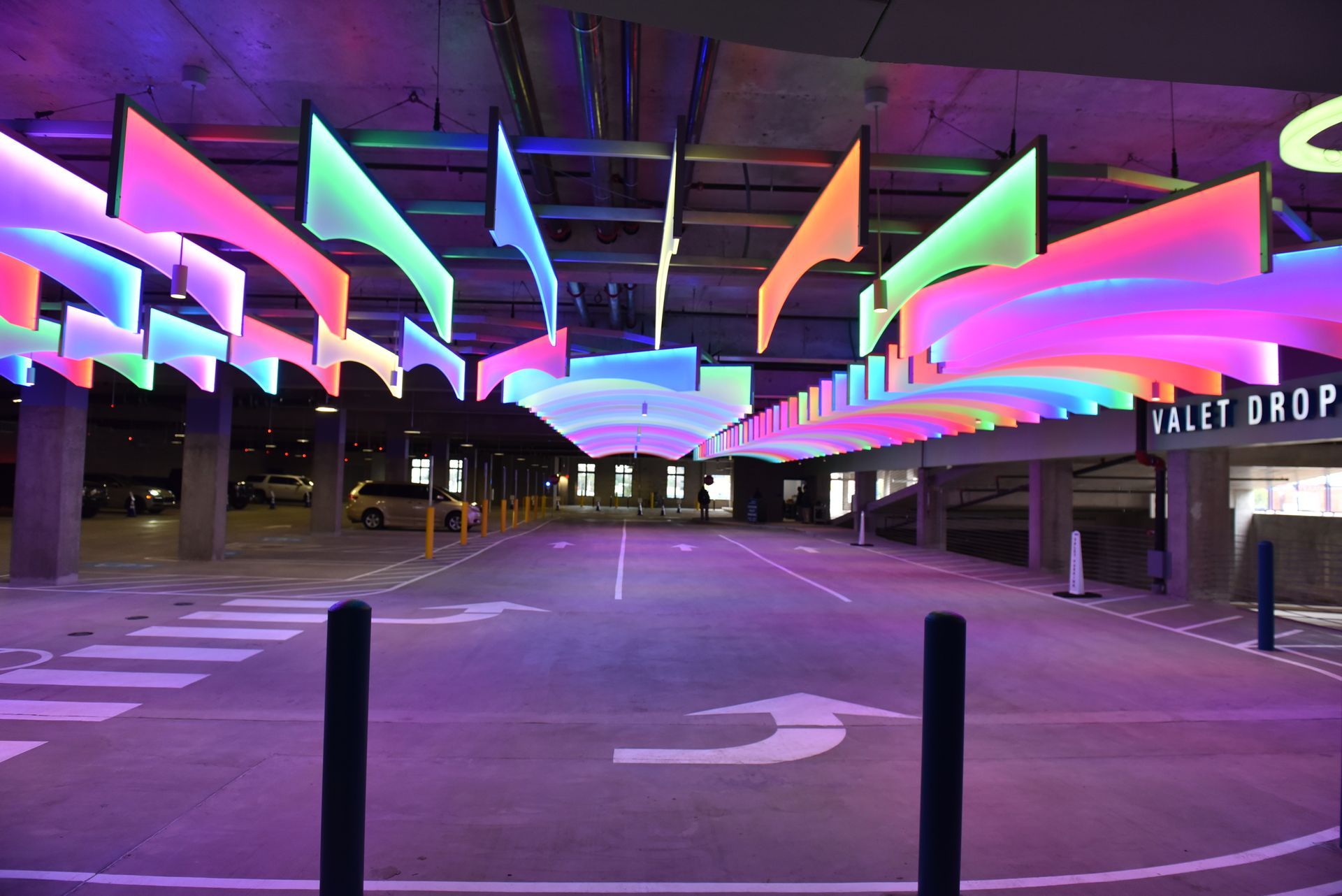 Colorful illuminated ribbons hanging above a parking garage valet area.