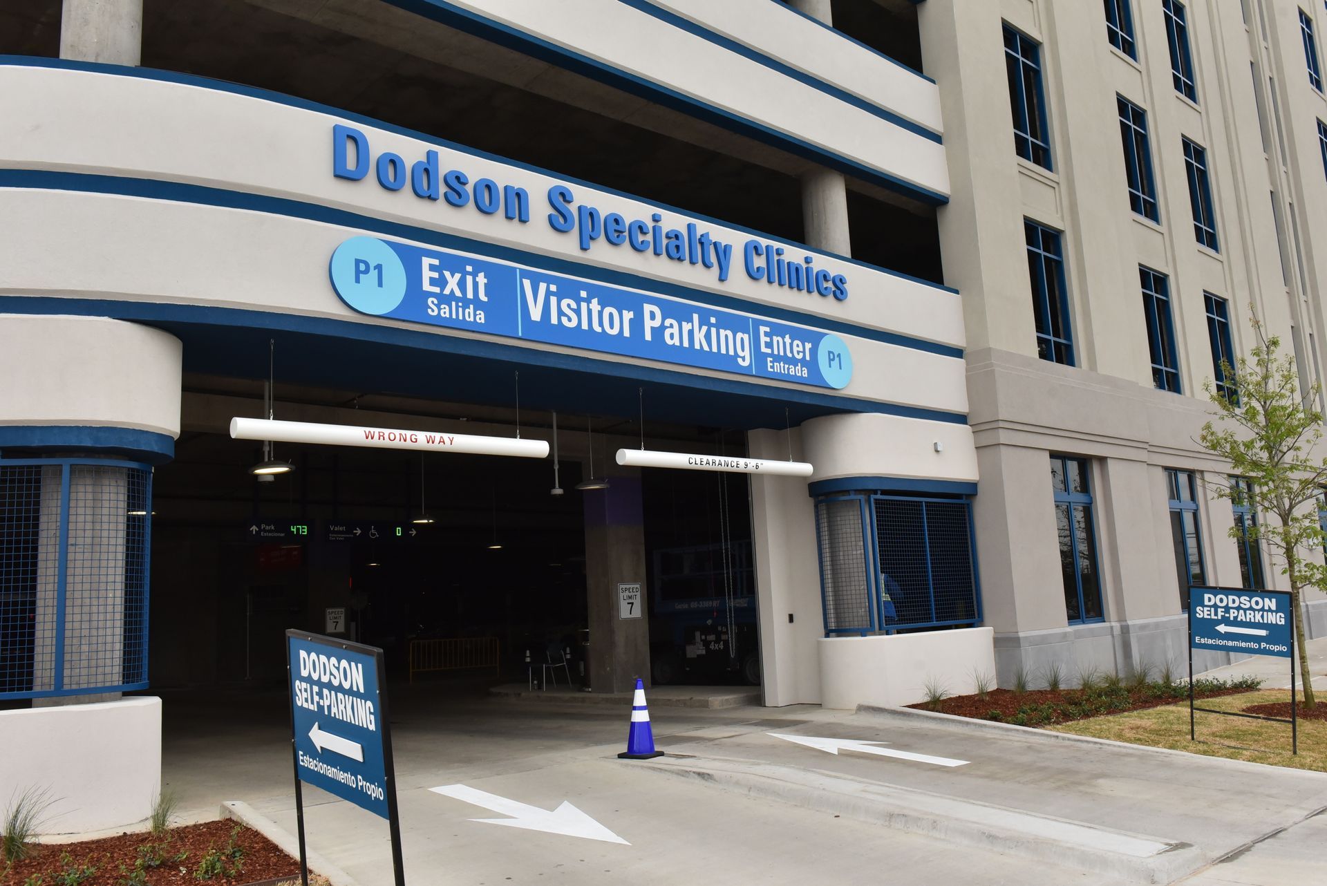 Entrance to Dodson Specialty Clinics visitor parking. White building, blue trim, sign, cars, cone.