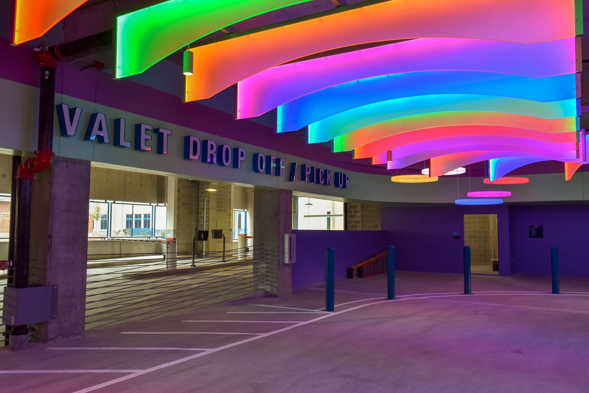 Valet drop-off area with rainbow-colored illuminated ceiling. Purple walls and white lane markings.