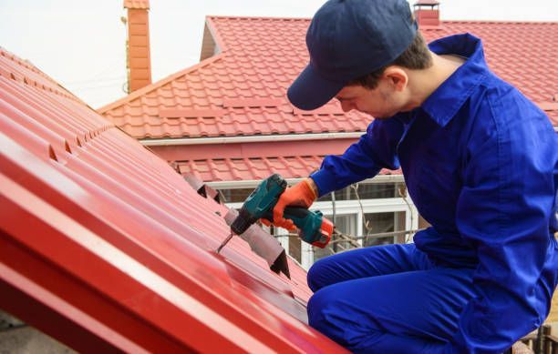 A man in blue overalls drills to install a metal roof, showcasing his skills as a roofing contractor.
