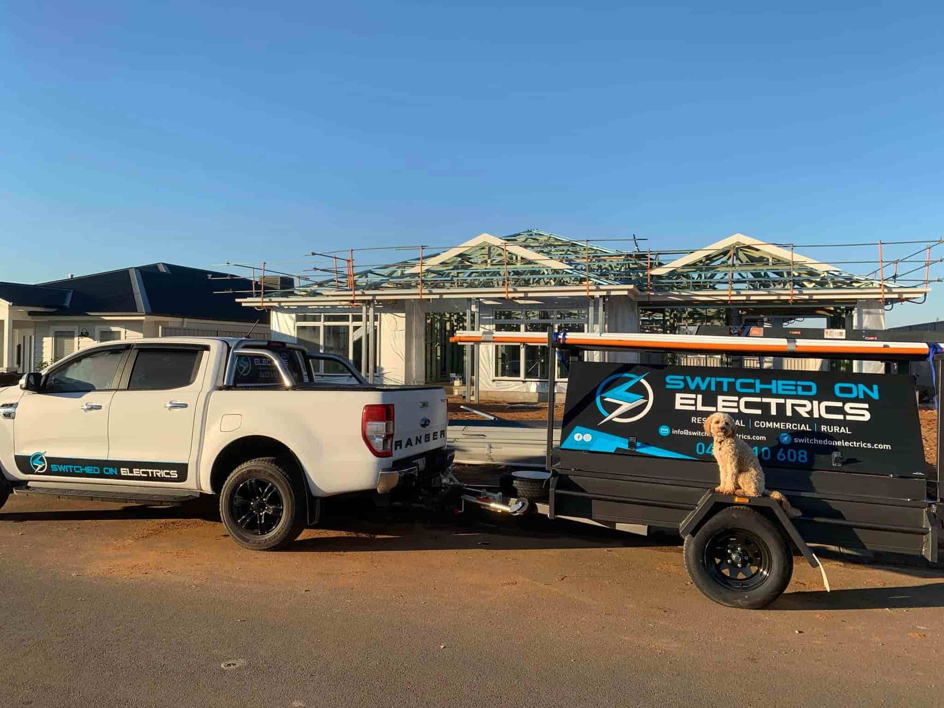 Switched On Electrics vehicle and trailer parked at residential construction site with visible roof 