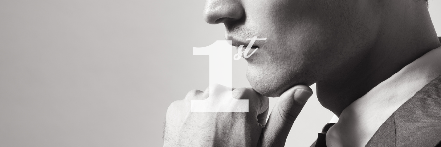 Man in suit with finger to lips, “1” superimposed. Black and white.