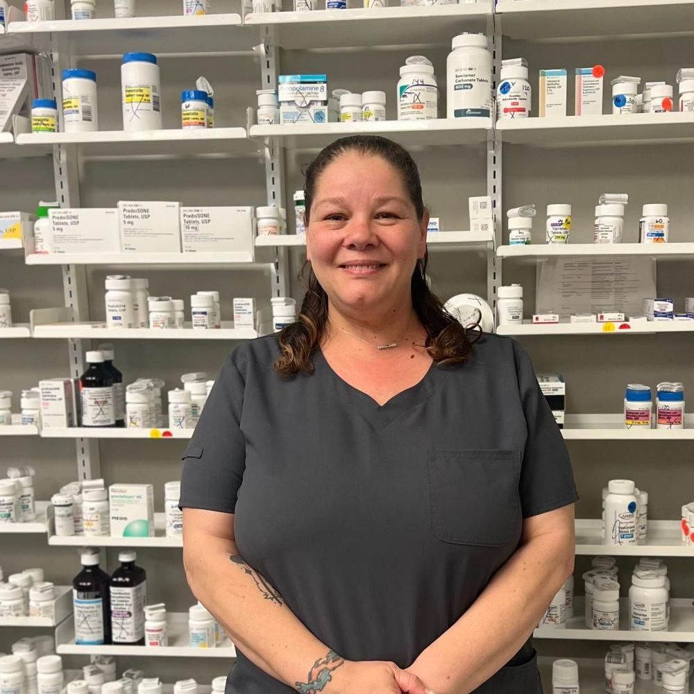 A woman is standing in front of a pharmacy filled with lots of bottles of medication.