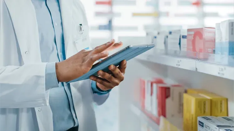 A pharmacist is looking at a tablet in a pharmacy.
