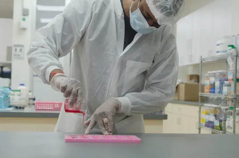 A man in a lab coat and mask is standing at a table in a lab.