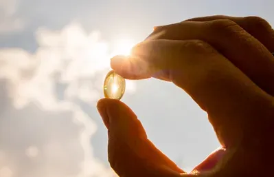 A person is holding a pill in their hand in front of the sun.