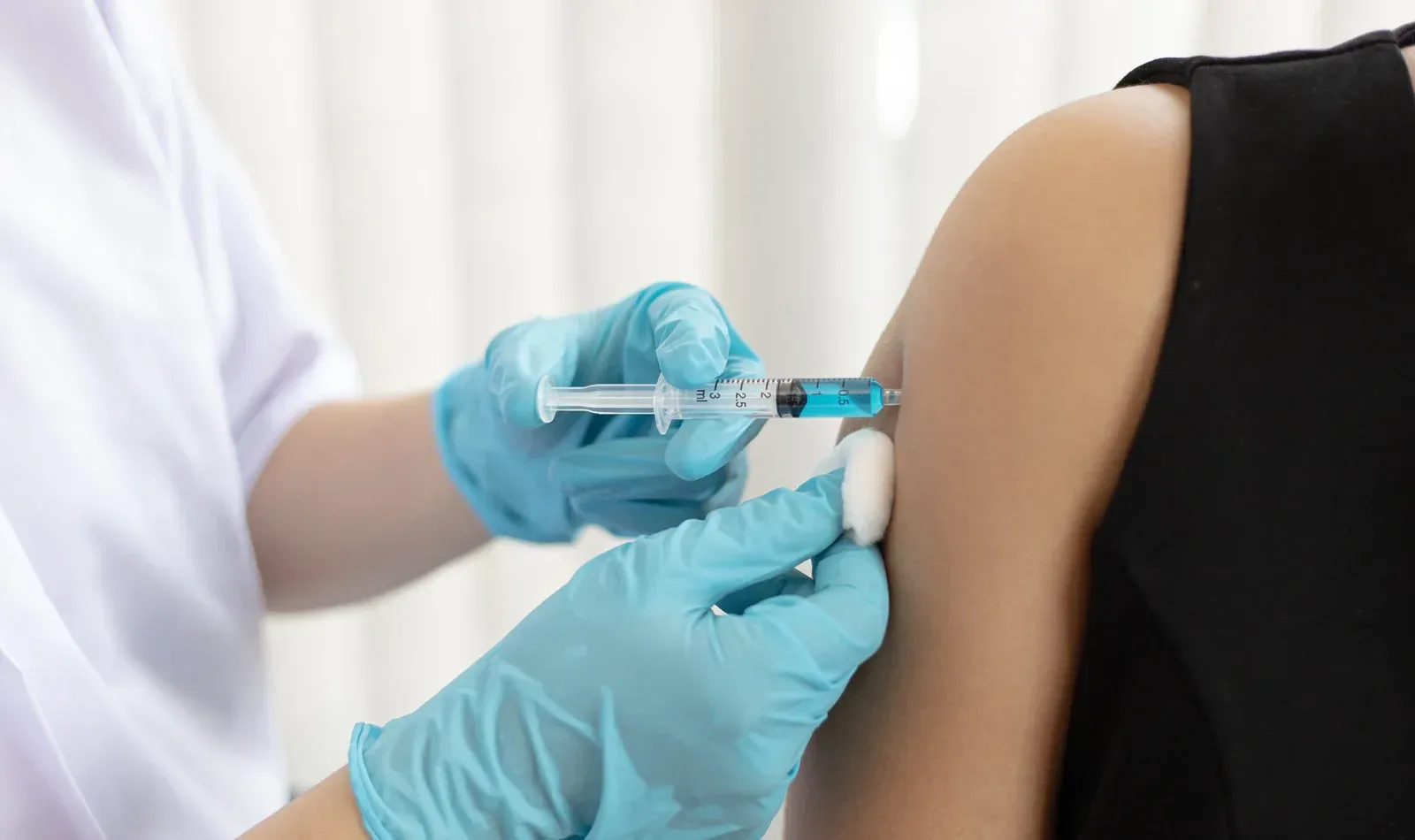 Person receiving a vaccine injection in their upper arm by a gloved healthcare worker.