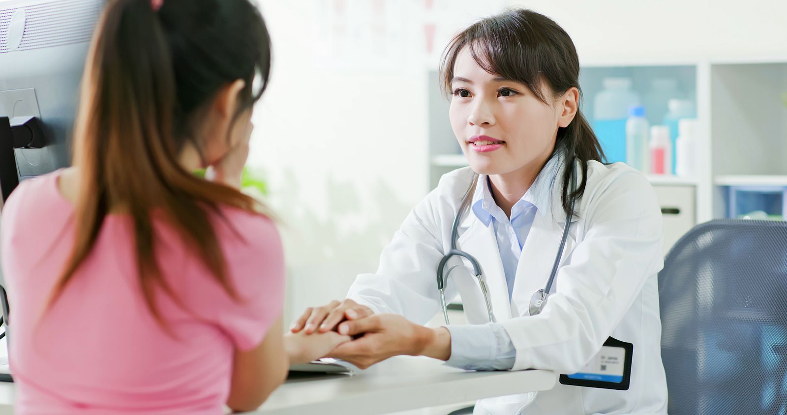 Doctor consulting a seated patient in a bright clinic office, with hand on the desk.