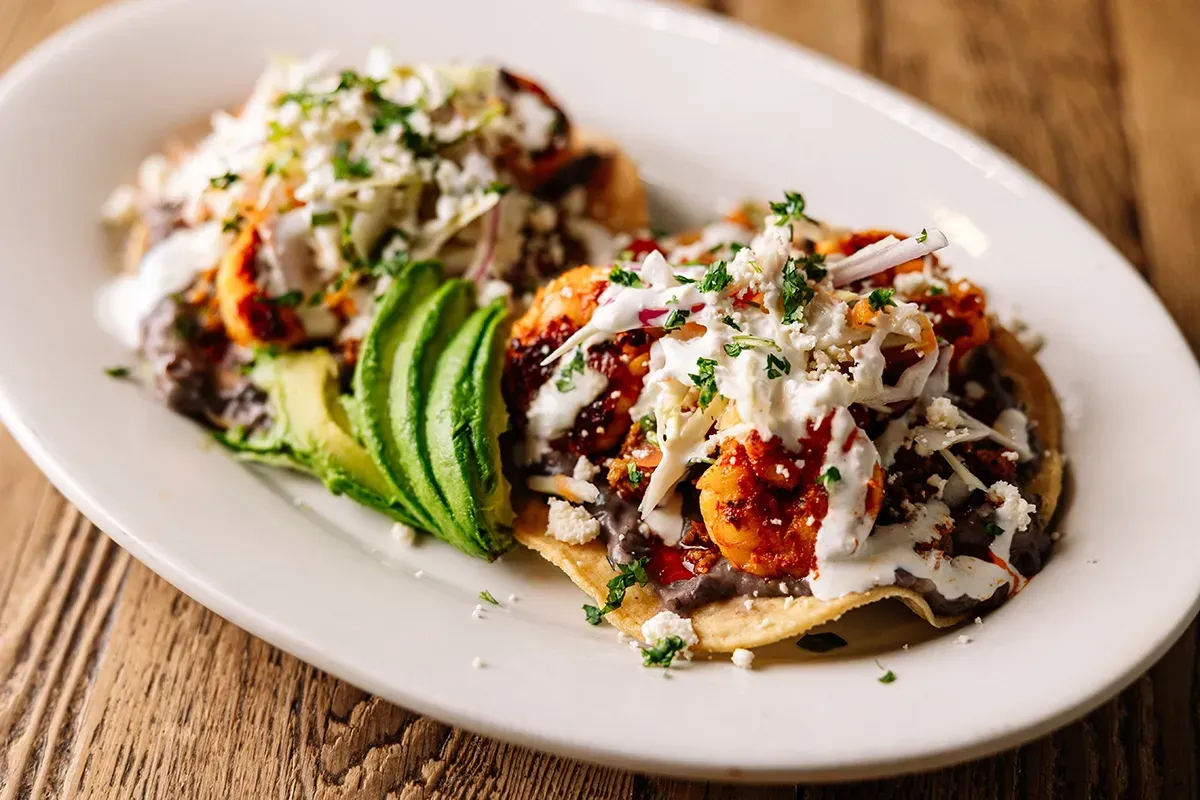 A plate of food with avocado and chorizo and shrimp on a wooden table.