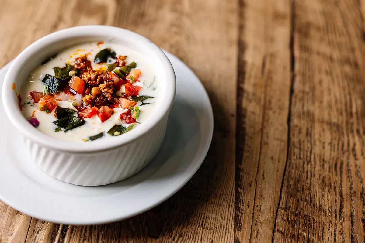 A bowl of Chorizo Con Queso on a white plate on a wooden table.