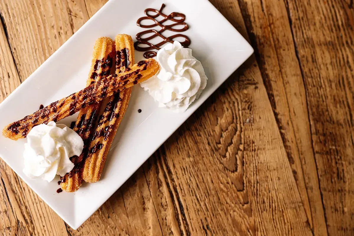 A white plate topped with churros and whipped cream on a wooden table.