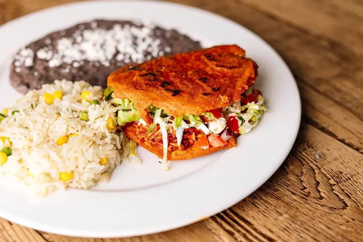 A plate of food with Gordita, rice and beans on a wooden table.