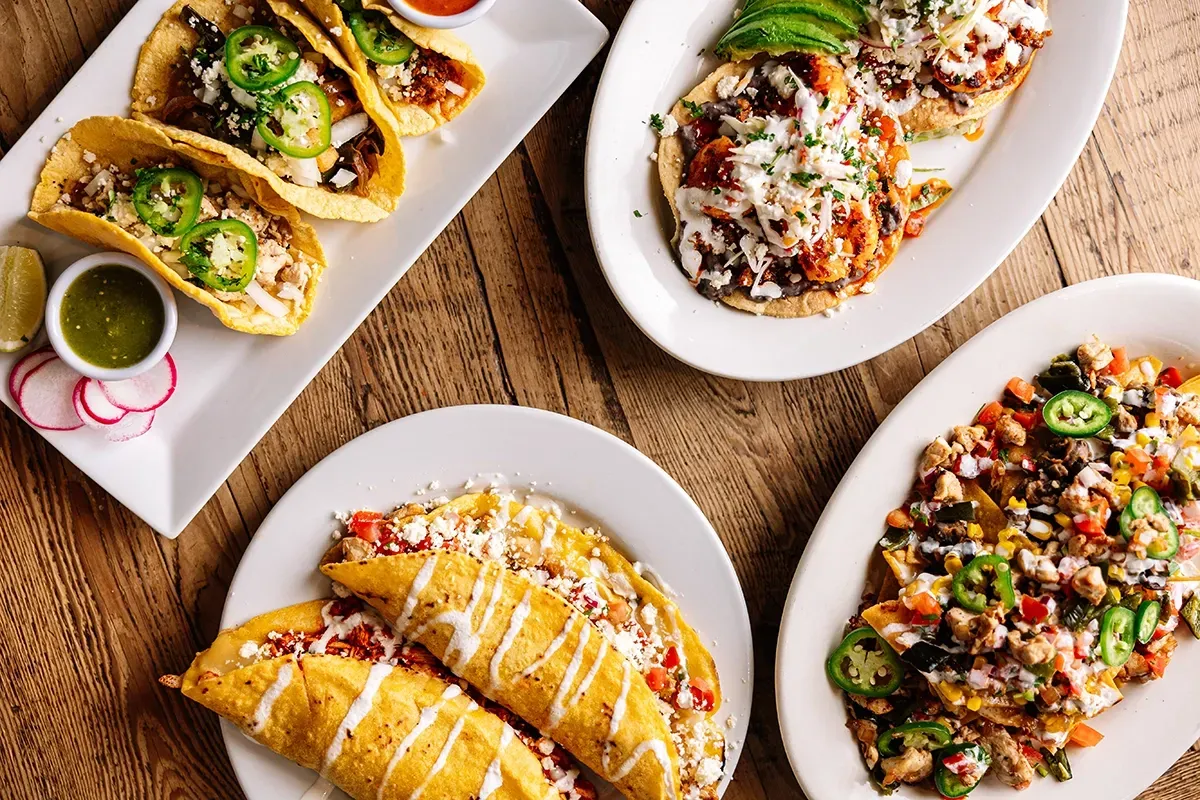 Four plates of food are sitting on a wooden table.