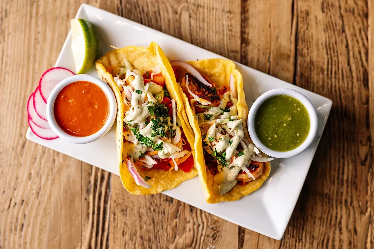 A white plate topped with two tacos and two dipping sauces on a wooden table.