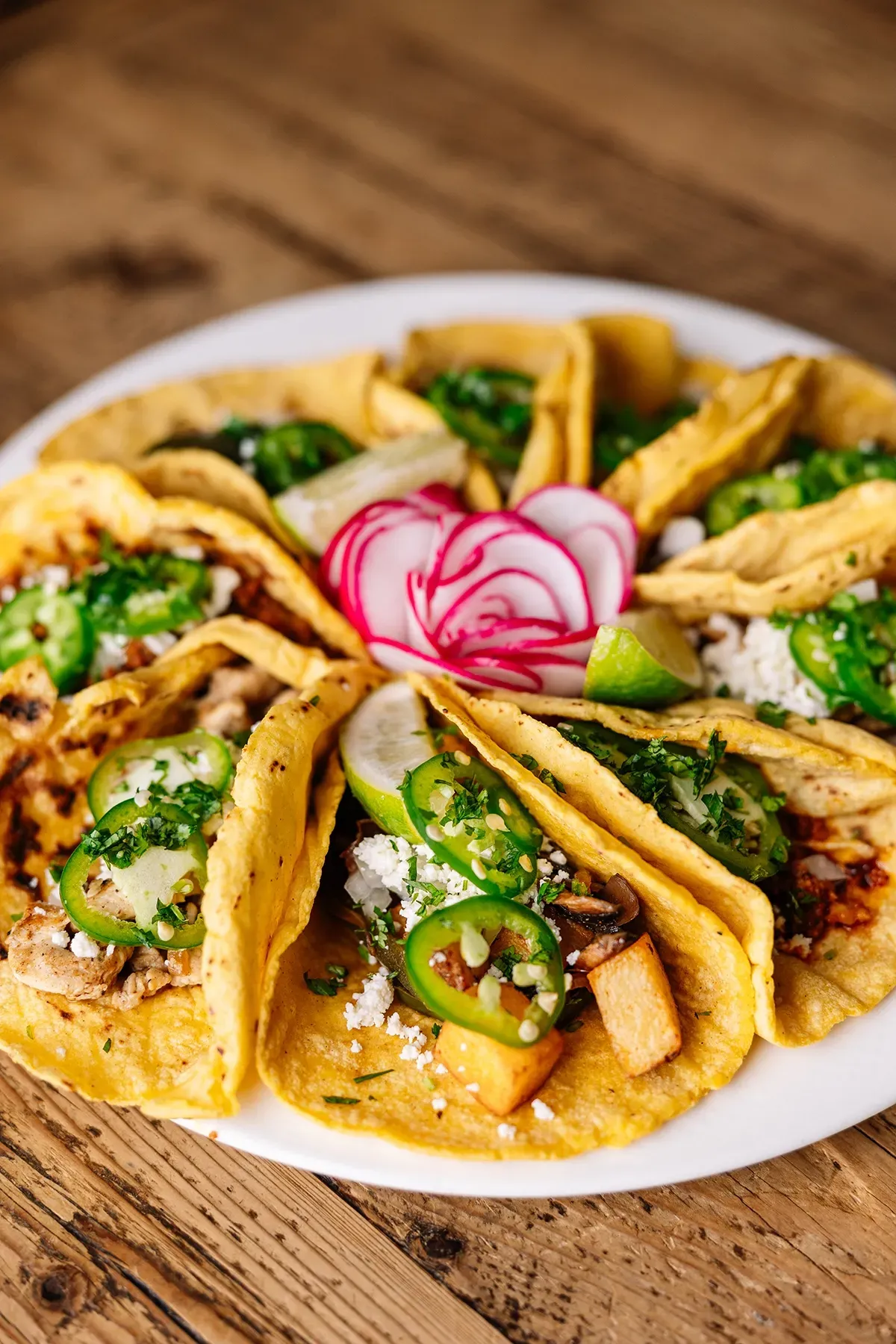 A white plate topped with tacos and vegetables on a wooden table.