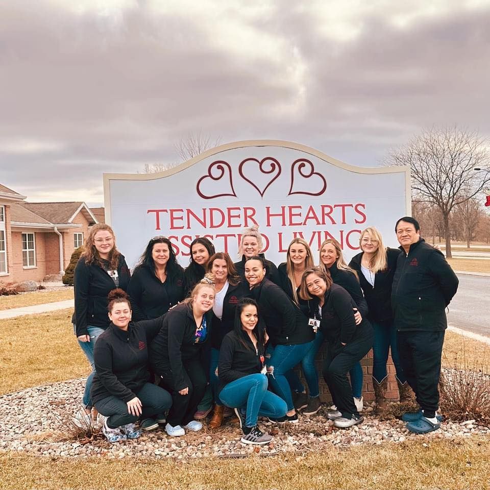 The Tender Hearts team is  posing for a picture in front of a tender hearts sign.