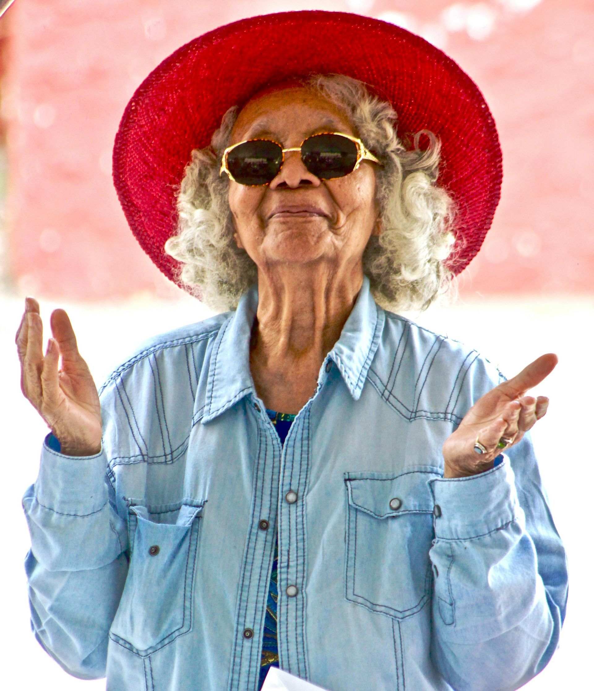 An elderly woman wearing a red hat and sunglasses