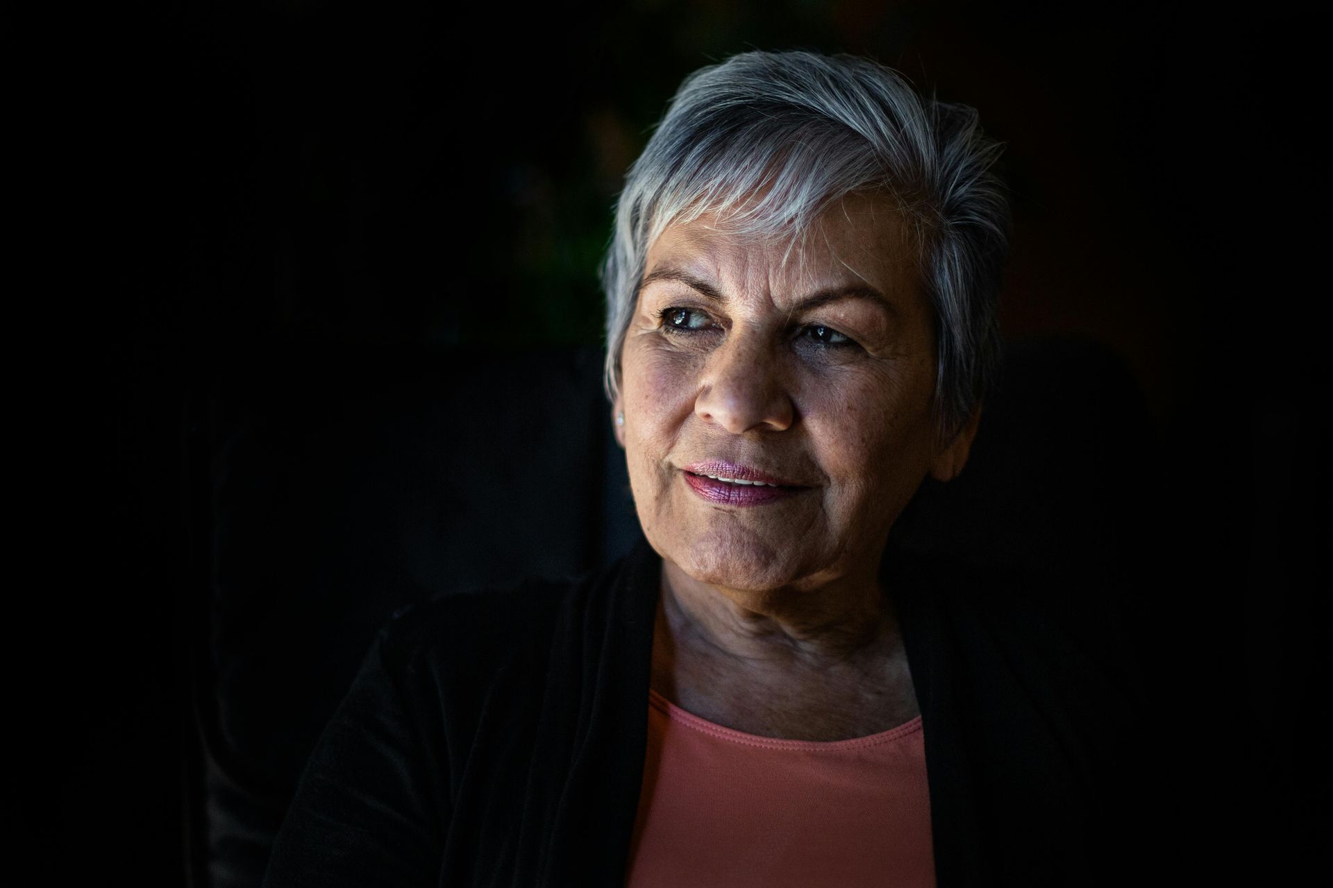 An older woman with gray hair is smiling in a dark room.