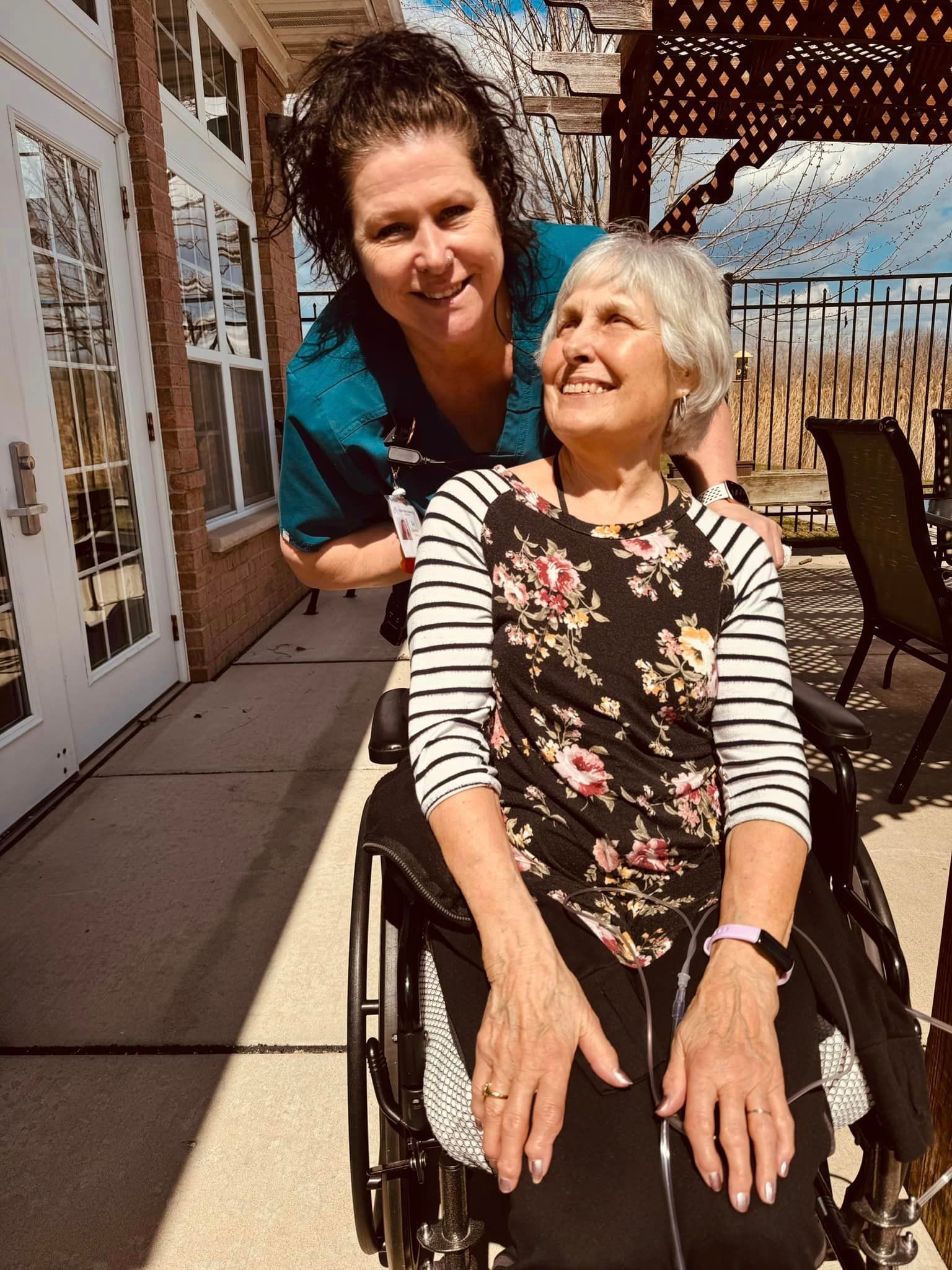 A nurse is putting her arm around an older woman in a wheelchair.