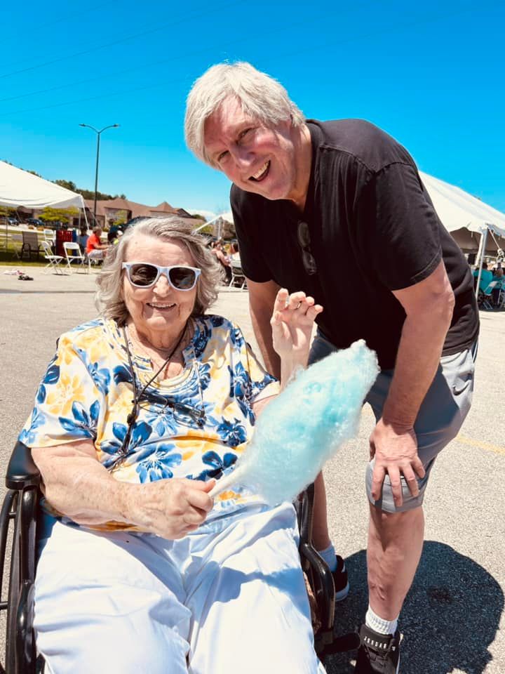 A man is standing next to a woman in a wheelchair holding cotton candy.