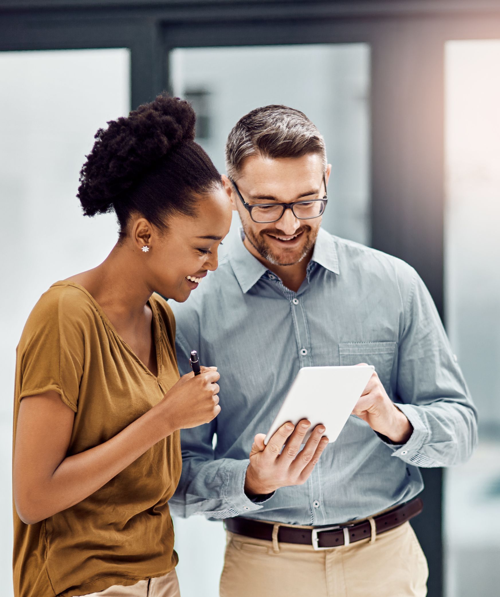 Woman and man smiling, looking at a tablet together in an office setting.