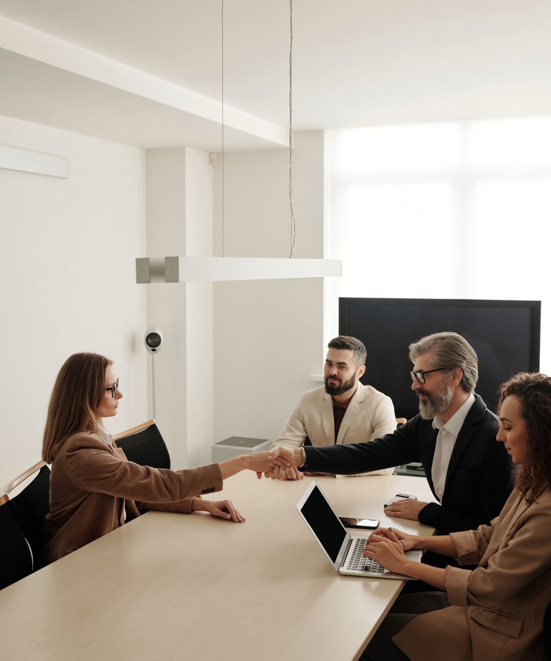 People shaking hands across a table in a modern office, likely a business agreement.