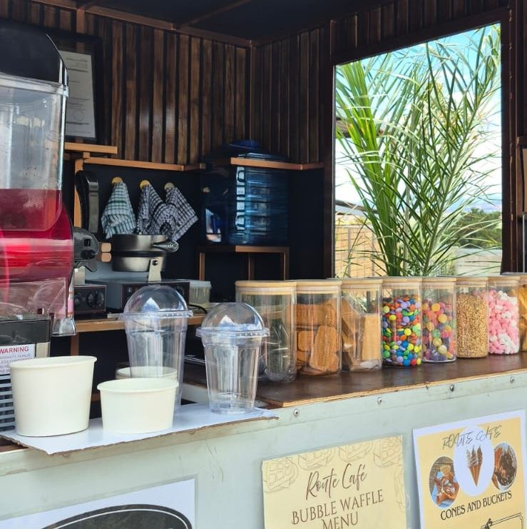Waffle shop counter with treats in jars, clear cups, and a red beverage dispenser.