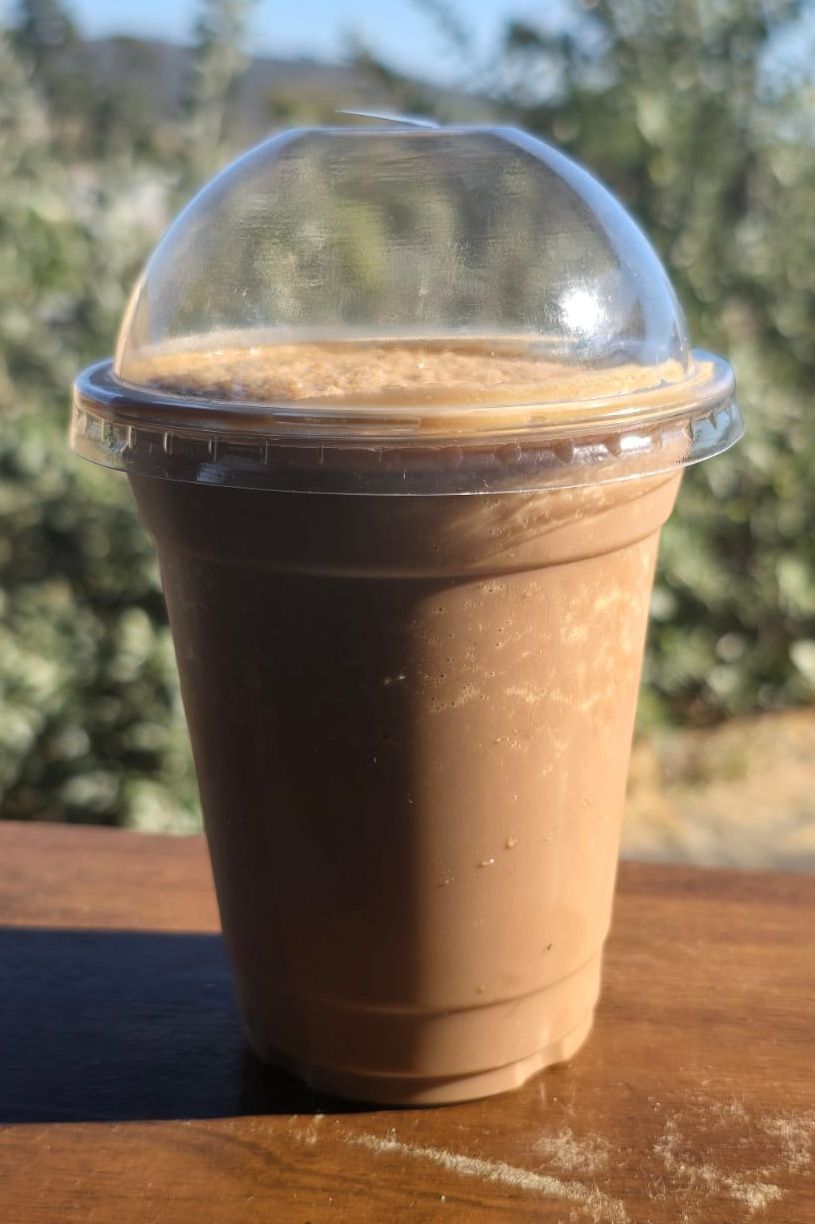 Iced coffee drink with whipped cream and chocolate drizzle, in a clear plastic cup with a dome lid and black straw.