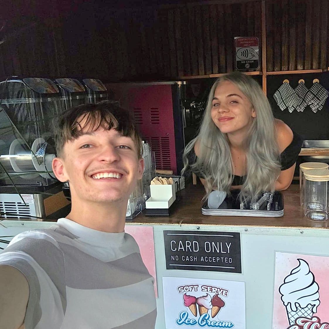 Smiling person taking a selfie with a person standing behind an ice cream counter.