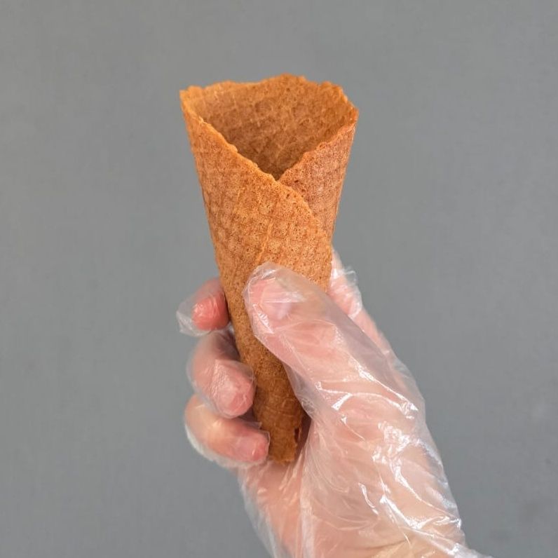 Hand in a clear glove holding an empty, brown waffle cone.