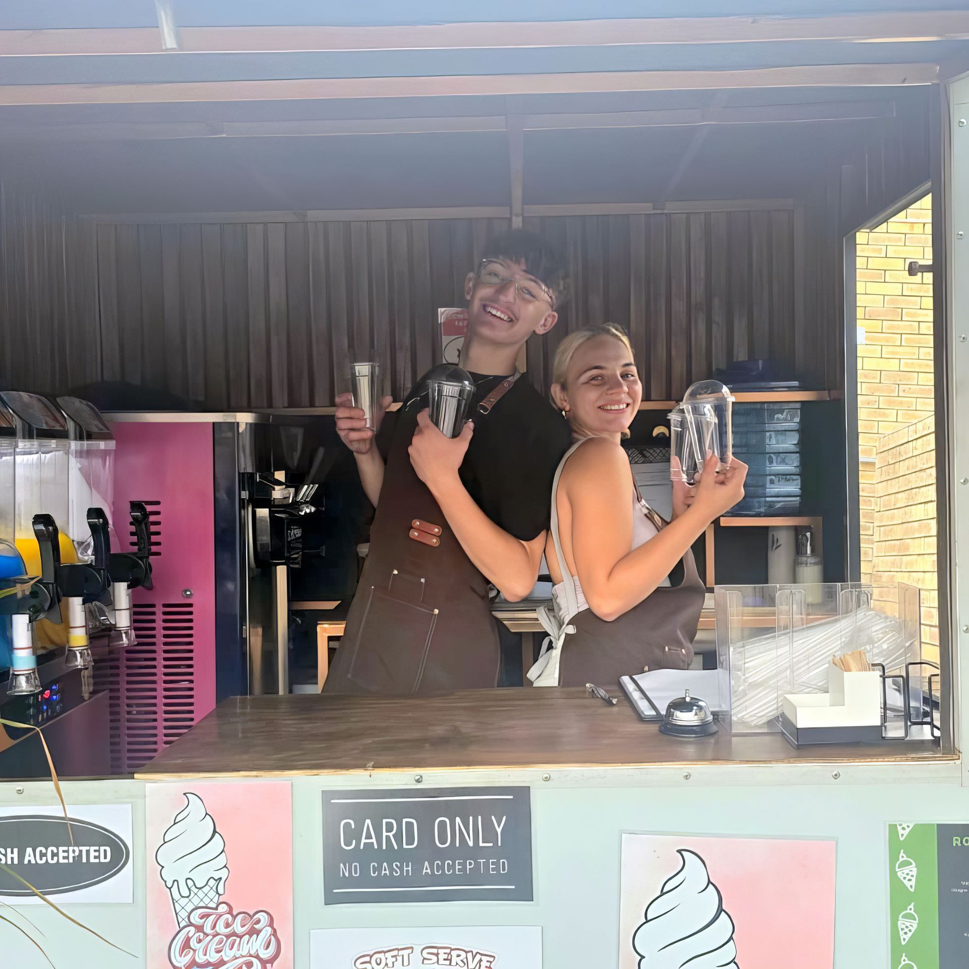 Two smiling people at a food stand, holding drinks. Pink accents and ice cream art are visible.