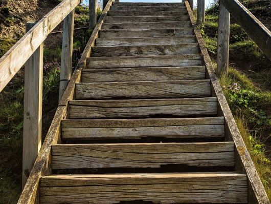 A wooden staircase with a railing going up a hill.