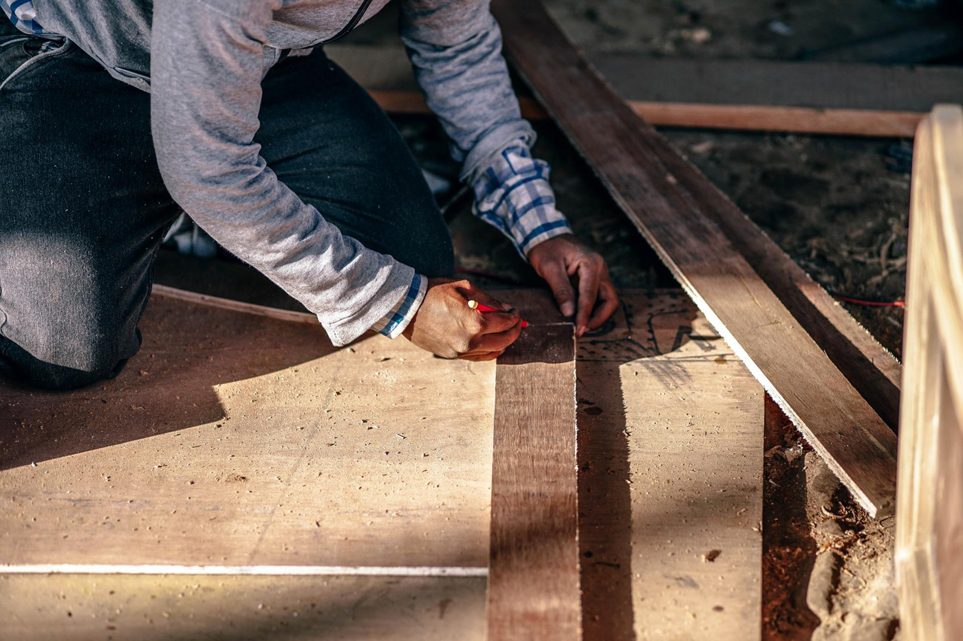 A man is measuring a piece of wood with a tape measure.