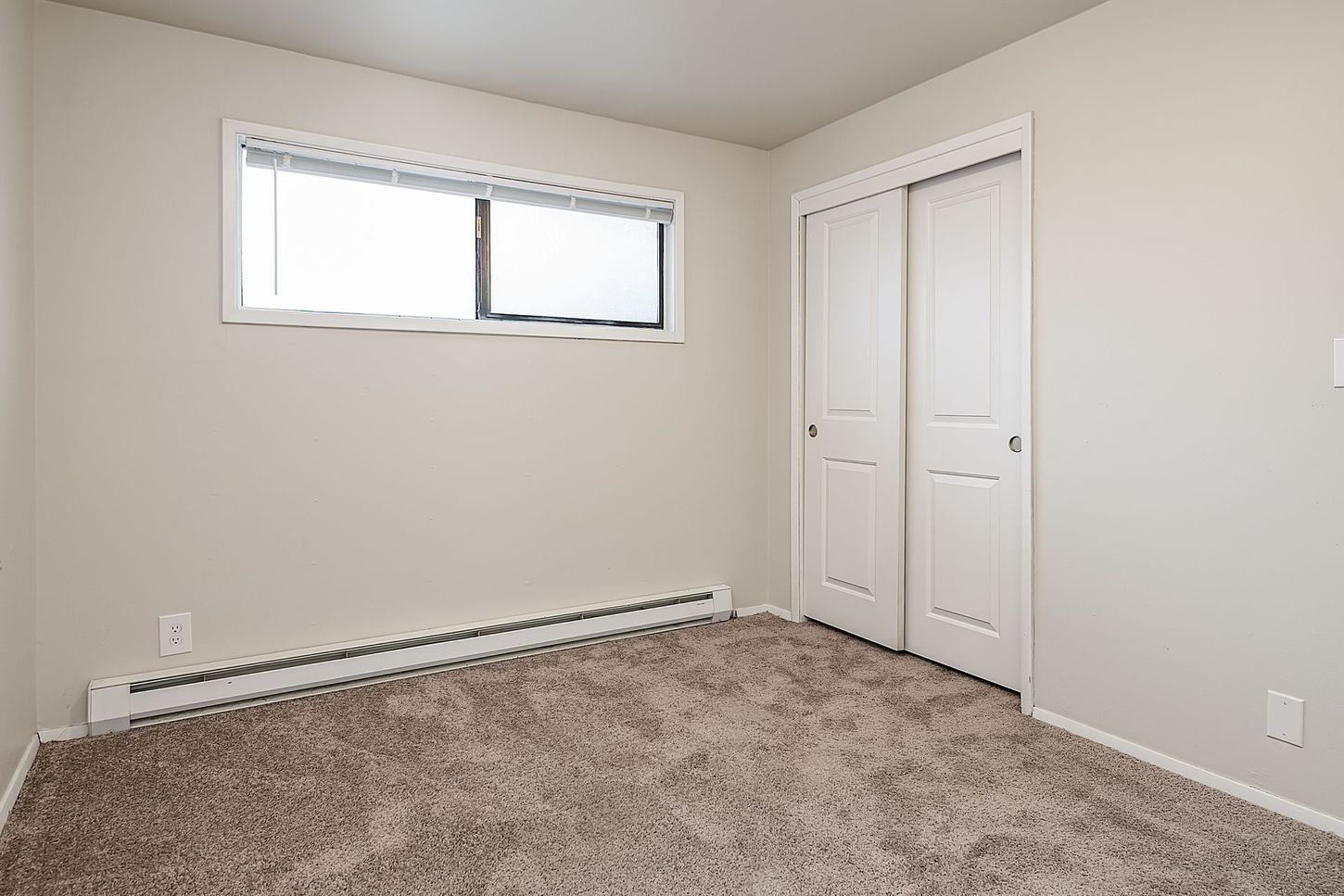 Photo showing a bedroom with a very long window higher on the wall, and dual closet doors