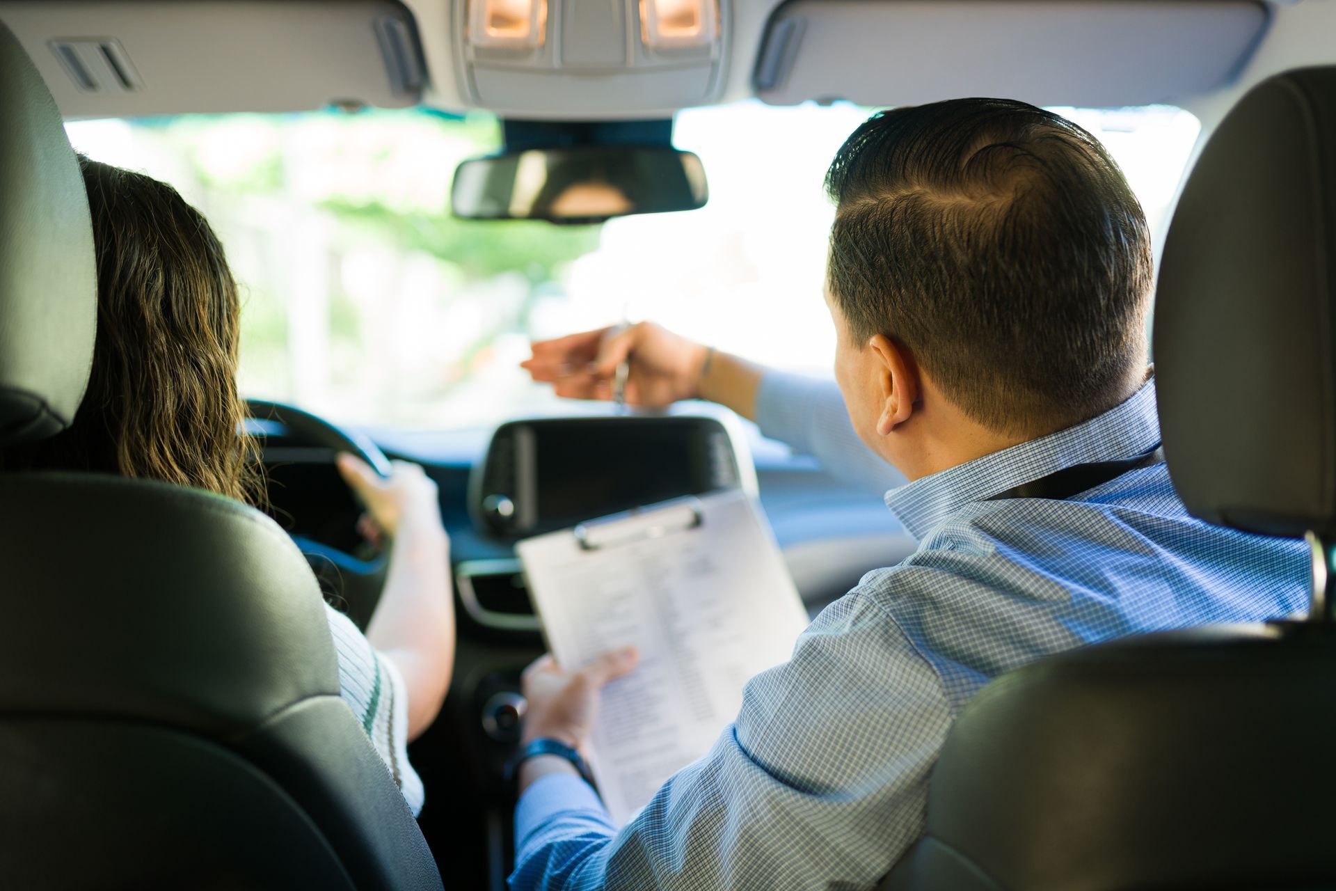 Driving instructor coaching a driver in a white car, outdoors with orange cones.