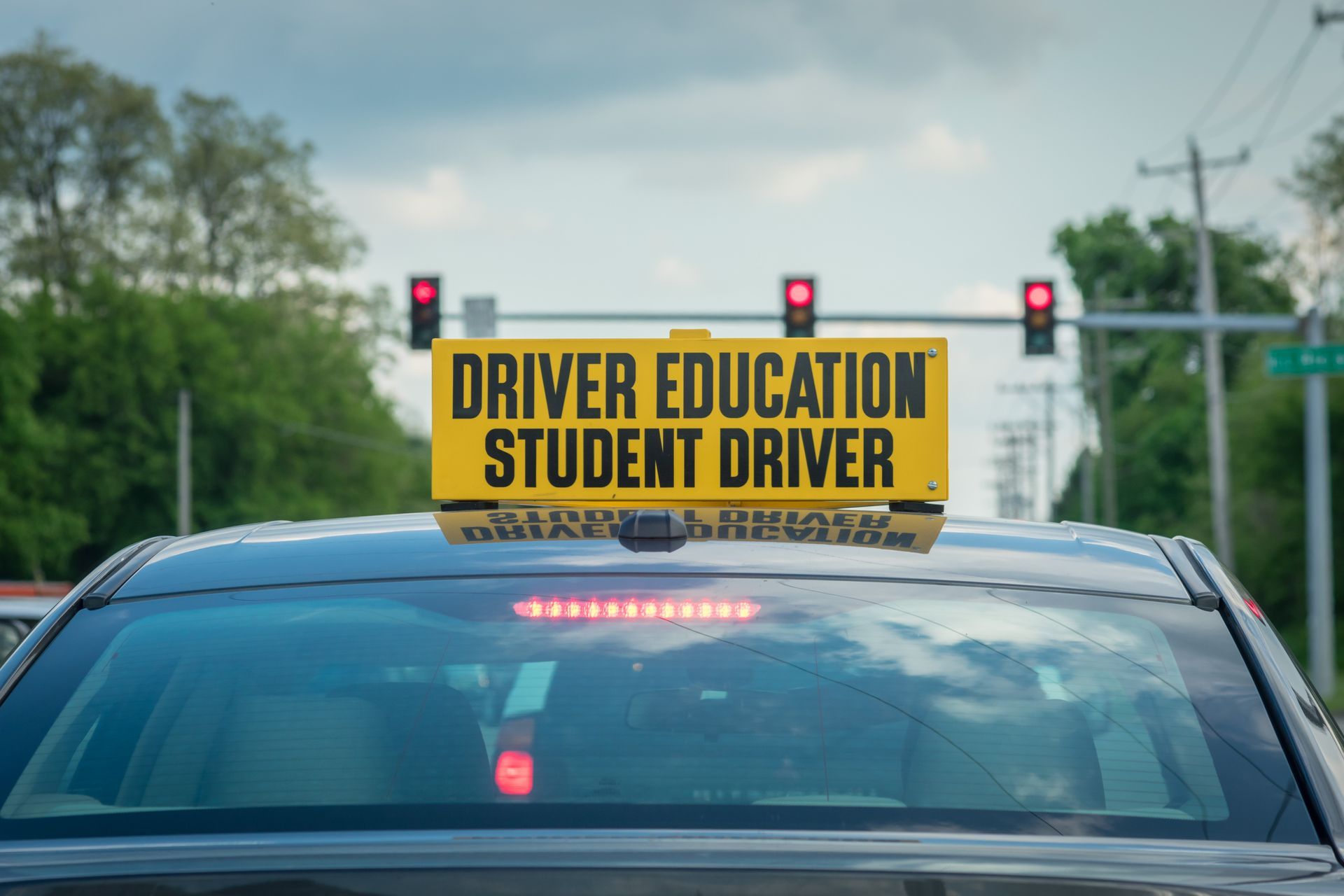 A woman driving a car with an instructor. Instructor smiling, holding a clipboard. Interior setting.