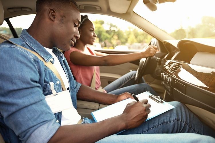 Woman and man shaking hands near a black car on a driving practice course.