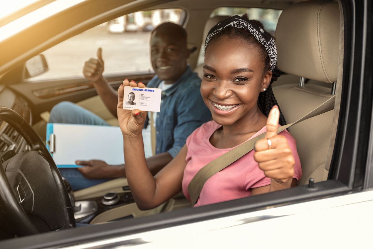 Man instructing a woman in a car. Man smiles, pointing, while woman drives, also smiling. Daytime setting.