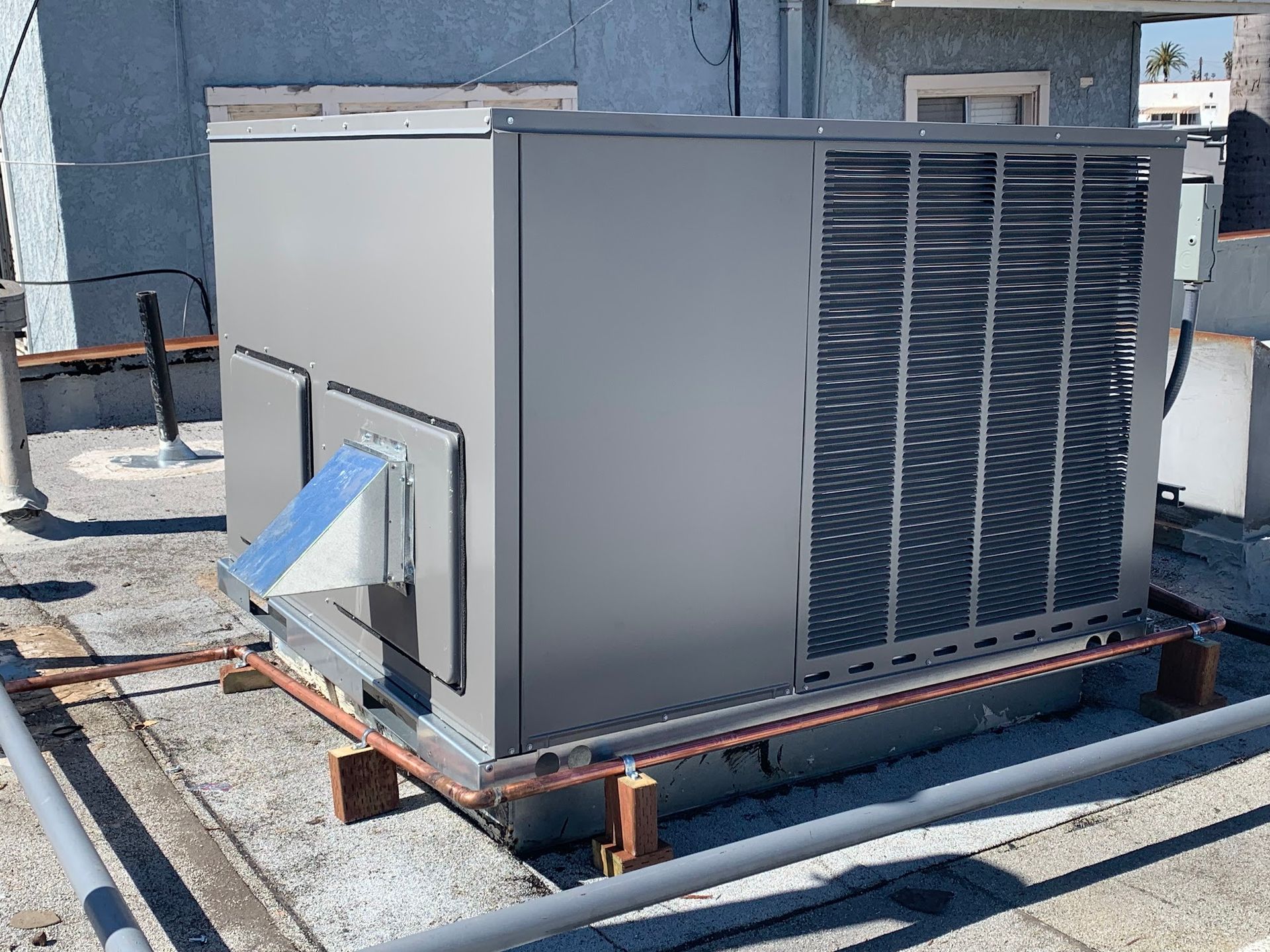 Gray rooftop HVAC unit on a building roof with copper piping.