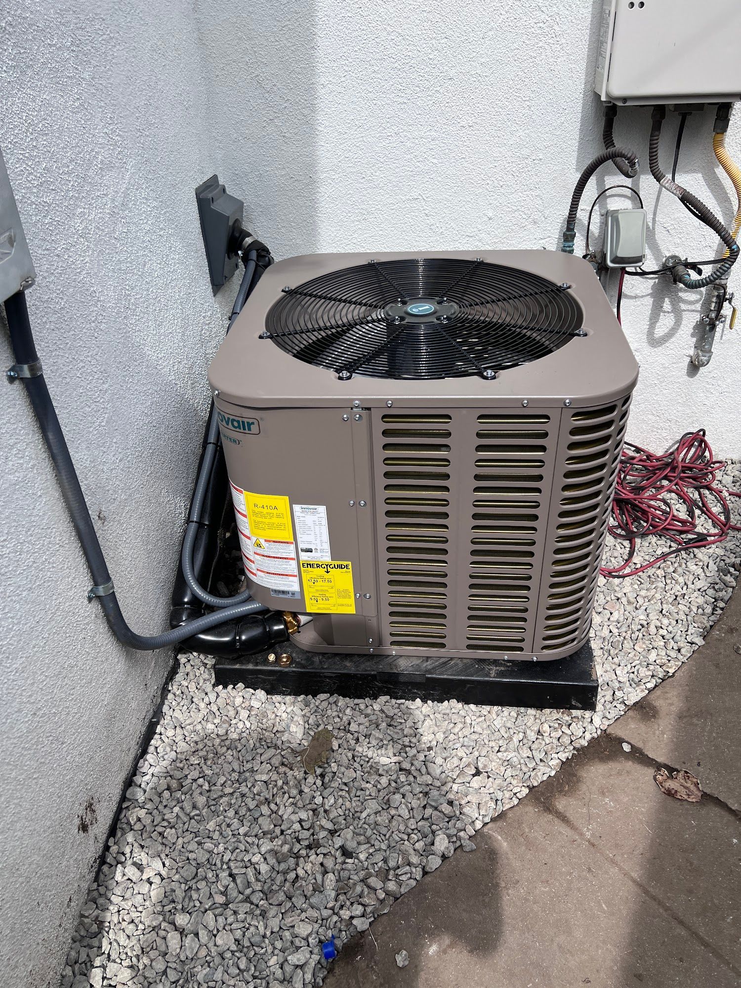 Air conditioning unit installed outside on a gravel bed, next to a building wall.