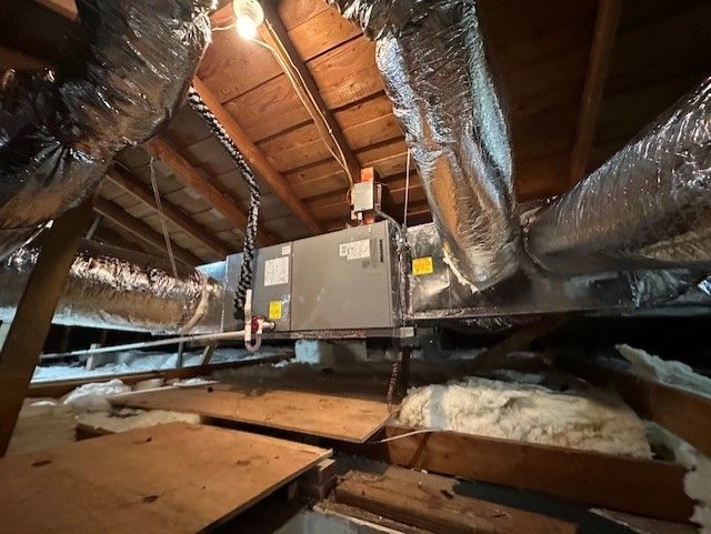 HVAC unit in an attic with ductwork, wooden beams, and insulation.
