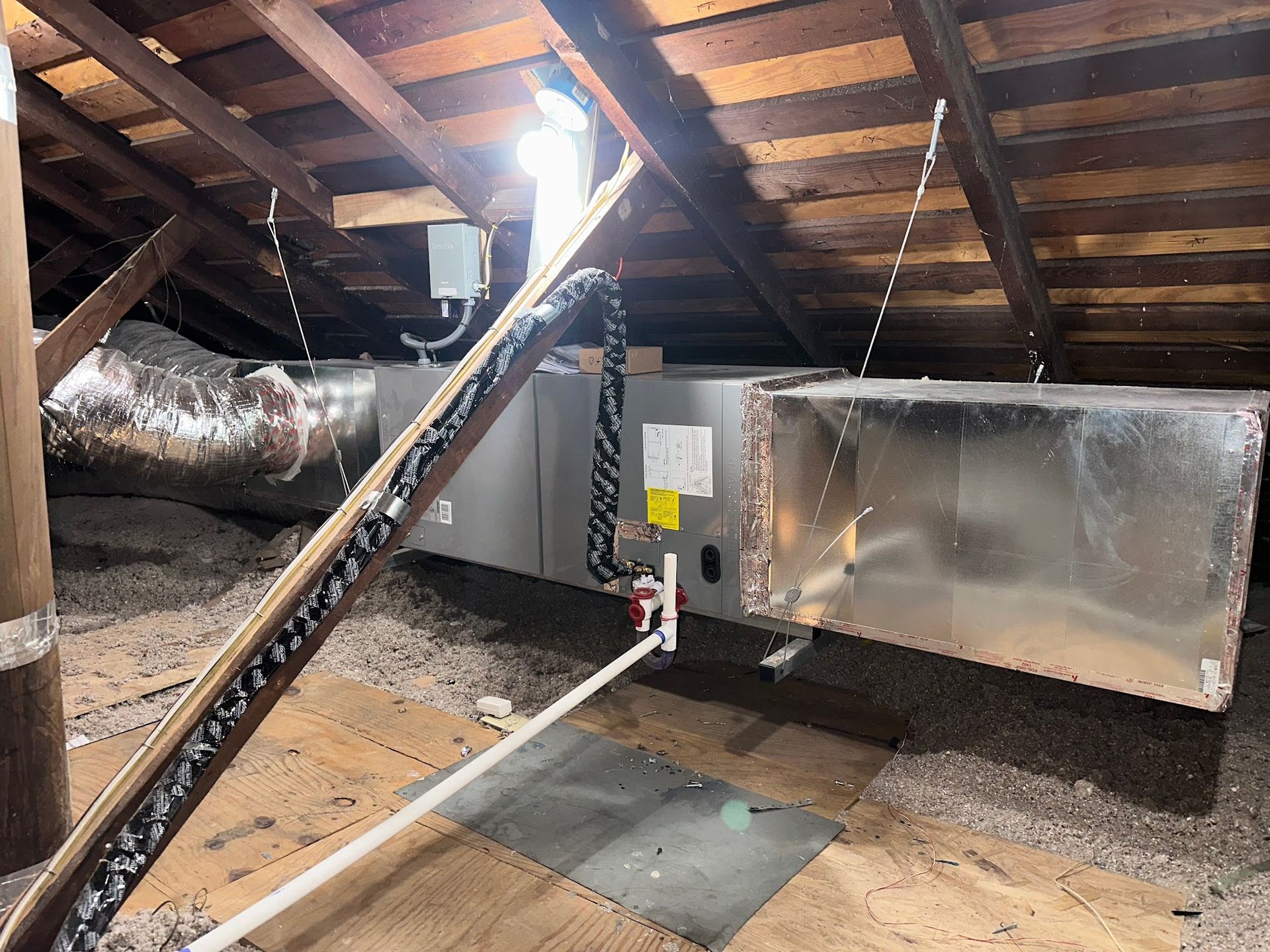 HVAC unit in an attic with ductwork, insulation, and exposed rafters.