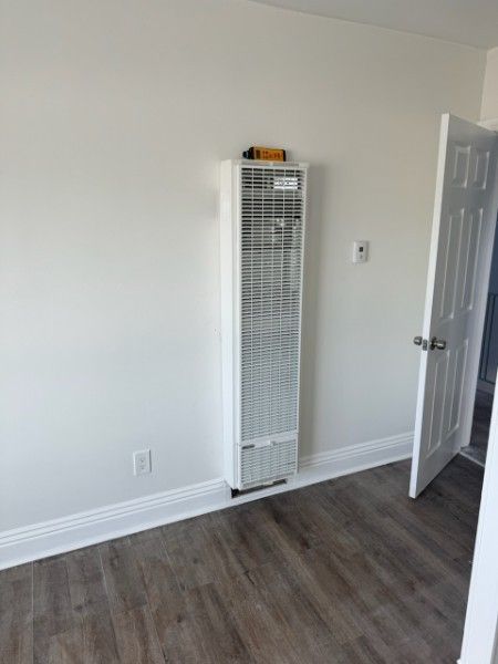 White wall heater on a white wall in a room with wood-look flooring and a white door.