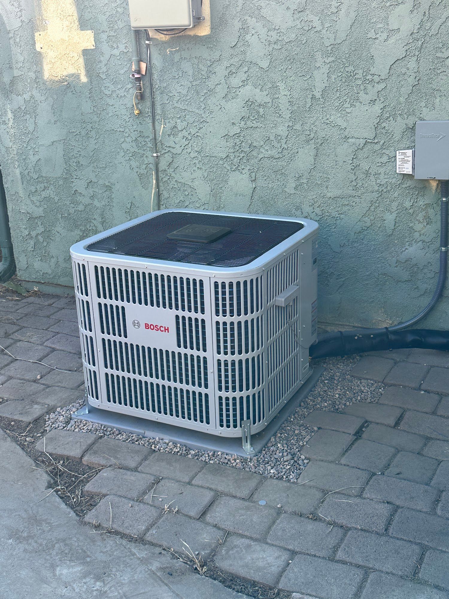 Gray air conditioning unit on brick ground against a stucco wall.